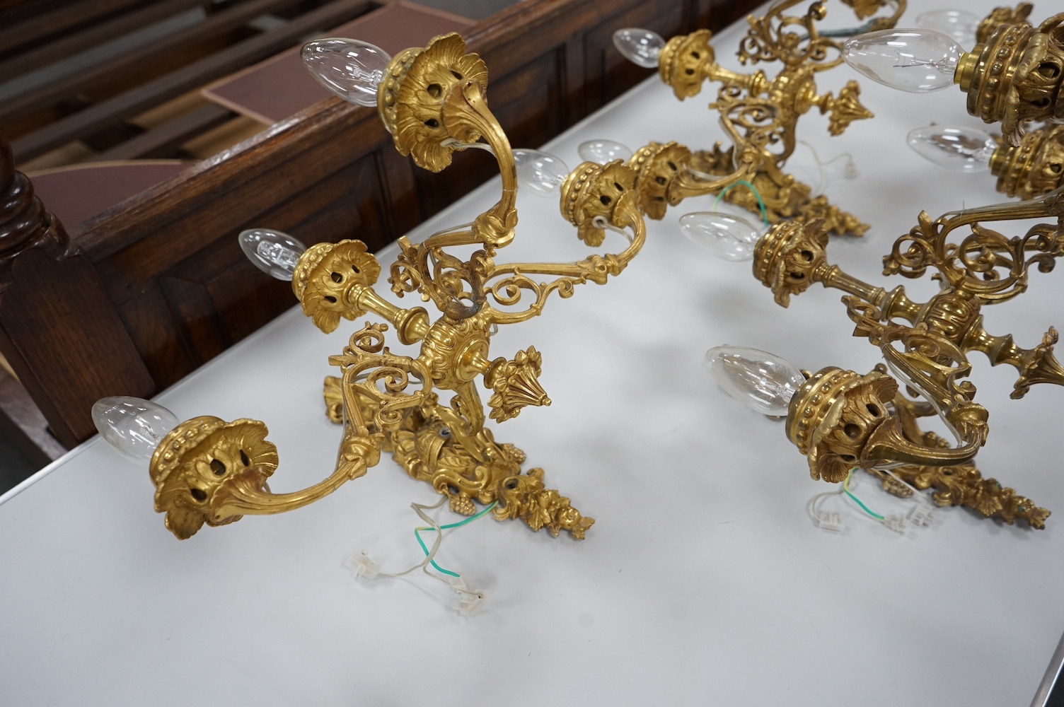 A set of four Baroque style, three branch brass wall lights. 44cm wide x 28cm high. Condition - good